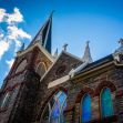 A perspective view of a stone church with a tall spire against a blue sky with clouds. A perspective view of a stone church with a tall spire against a blue sky with clouds.