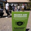 Signage at a public location indicating that masks are recommended, with people walking by. Signage at a public location indicating that masks are recommended, with people walking by.