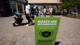 Signage at a public location indicating that masks are recommended, with people walking by.