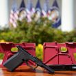 Ghost gun parts and assembly kits displayed on a table, with the U.S. flag in the background. Ghost gun parts and assembly kits displayed on a table, with the U.S. flag in the background.