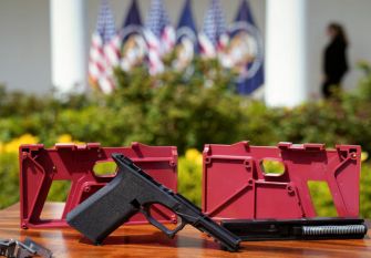 Ghost gun parts and assembly kits displayed on a table, with the U.S. flag in the background.