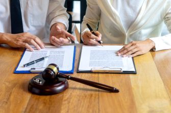 Two individuals discussing and signing contracts at a table, with a gavel in the foreground.