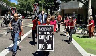 A group of protesters marches in downtown Portland, holding signs that read "Multnomah County vs Big Oil" as they advocate against oil and gas companies.