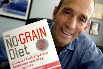 An osteopathic physician holding a book titled "The No-Grain Diet."