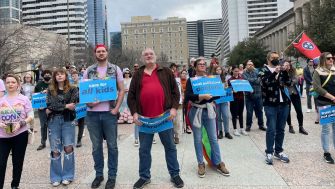 A group of people gathered in an outdoor setting holding signs advocating for gender-affirming care for minors.