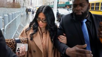 Jen Shah, a reality TV star, arrives at court with an escort, wearing sunglasses and a tan coat, amid her sentencing for telemarketing fraud.