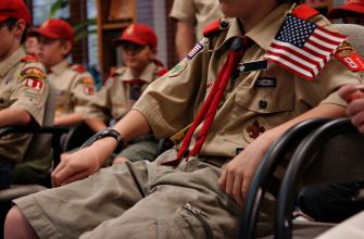 A group of Boy Scouts sitting together, wearing uniforms and hats, during a meeting or event.