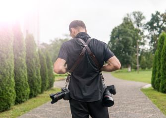 A photographer walking down a path wearing camera equipment.