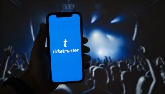 A person holding a smartphone displaying the Ticketmaster logo in front of a concert crowd.