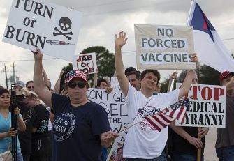 Protesters holding signs against vaccine mandates outside a hospital.