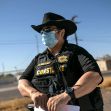 A law enforcement officer in a cowboy hat and face mask stands outside, overseeing a situation related to evictions. A law enforcement officer in a cowboy hat and face mask stands outside, overseeing a situation related to evictions.