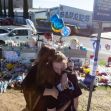 Two teenagers embrace in front of a memorial at Saugus High School, surrounded by flowers and balloons, honoring victims of a school shooting. Two teenagers embrace in front of a memorial at Saugus High School, surrounded by flowers and balloons, honoring victims of a school shooting.