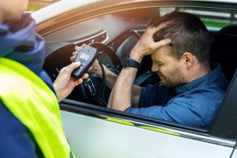 An officer administering a breathalyzer test to a distressed driver in a vehicle.