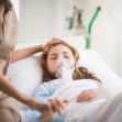 A young girl in a hospital bed receiving medical care with an oxygen mask, indicating a serious health condition. A young girl in a hospital bed receiving medical care with an oxygen mask, indicating a serious health condition.