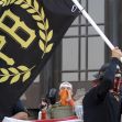 A group of individuals at a protest holding a black flag with the initials "PB" representing the Proud Boys organization. A group of individuals at a protest holding a black flag with the initials "PB" representing the Proud Boys organization.