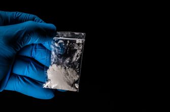 A gloved hand holding a small bag of white powder, suggesting illegal drug activity.