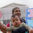 A woman holding a baby and a sign that reads "AMERICAN BORN CHILDREN ARE AMERICAN CHILDREN," with a small American flag, outside a courthouse. A woman holding a baby and a sign that reads "AMERICAN BORN CHILDREN ARE AMERICAN CHILDREN," with a small American flag, outside a courthouse.