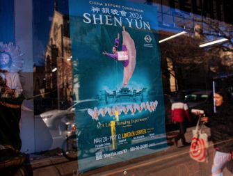 Promotional poster for Shen Yun 2024, showcasing a dancer in traditional attire, displayed in a storefront window.
