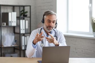 A physician wearing a headset, engaged in a telemedicine consultation via laptop.