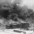 Black smoke billows over the buildings of Tulsa during the 1921 Race Massacre, illustrating the extent of the destruction in the Greenwood district, known as "Black Wall Street." Black smoke billows over the buildings of Tulsa during the 1921 Race Massacre, illustrating the extent of the destruction in the Greenwood district, known as "Black Wall Street."