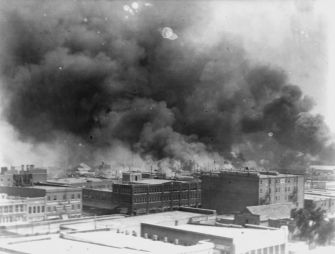 Black smoke billows over the buildings of Tulsa during the 1921 Race Massacre, illustrating the extent of the destruction in the Greenwood district, known as "Black Wall Street."