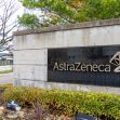 A sign displaying the AstraZeneca logo at their corporate headquarters, surrounded by landscaping. A sign displaying the AstraZeneca logo at their corporate headquarters, surrounded by landscaping.