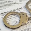 Handcuffs resting on a 1040 U.S. Individual Income Tax Return form, symbolizing tax fraud and legal repercussions. Handcuffs resting on a 1040 U.S. Individual Income Tax Return form, symbolizing tax fraud and legal repercussions.