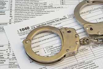Handcuffs resting on a 1040 U.S. Individual Income Tax Return form, symbolizing tax fraud and legal repercussions.