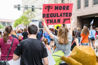 Protesters holding signs advocating for abortion rights, with one sign reading "More Regulated Than Guns."