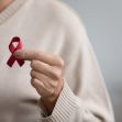 A person holding a red ribbon, symbolizing awareness and support for HIV/AIDS. A person holding a red ribbon, symbolizing awareness and support for HIV/AIDS.