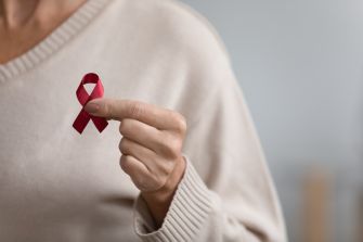 A person holding a red ribbon, symbolizing awareness and support for HIV/AIDS.