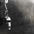 A metallic whistle hanging against a textured background. A metallic whistle hanging against a textured background.