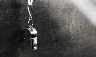 A metallic whistle hanging against a textured background.