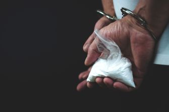 A hand holding a bag of white powdery substance while wearing handcuffs.
