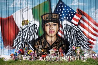 A mural depicting a soldier with wings, surrounded by flags and a memorial of flowers and candles.