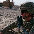 A soldier communicating via radio in a military setting, with a vehicle in the background. A soldier communicating via radio in a military setting, with a vehicle in the background.