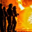 Firefighters in training during a simulated emergency response, with flames in the background. Firefighters in training during a simulated emergency response, with flames in the background.