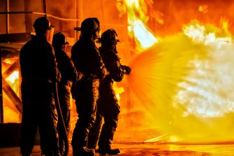 Firefighters in training during a simulated emergency response, with flames in the background.