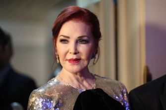 Priscilla Presley at a public event, wearing a sparkling outfit and looking seriously into the camera.