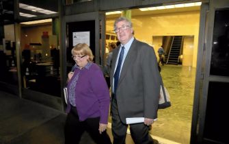 A couple exiting a courthouse, one wearing a purple jacket and the other in a suit and tie.