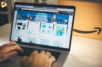 A person navigating the Amazon Prime Day webpage on a laptop, with an Amazon package in the background.