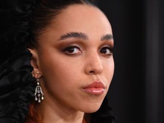 Close-up portrait of musician FKA Twigs, featuring dramatic makeup and ornate earrings.