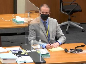 Former police officer Derek Chauvin sitting at a courtroom table during the George Floyd death trial, wearing a mask and taking notes.