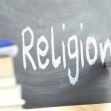 A hand writing "Religion" on a chalkboard, with books in the foreground. A hand writing "Religion" on a chalkboard, with books in the foreground.