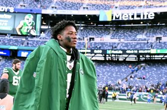 Ahmad "Sauce" Gardner walking on the field of MetLife Stadium, wearing a green hooded cape.