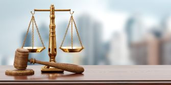 A wooden gavel and a balanced scale symbolizing justice on a desk with a blurred urban background.