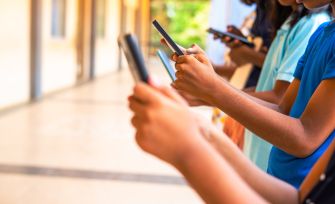 Group of children using smartphones while standing in a hallway.