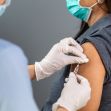 A healthcare professional administering a vaccine to a patient wearing a mask. A healthcare professional administering a vaccine to a patient wearing a mask.