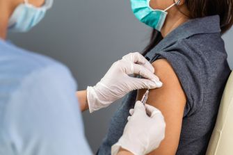A healthcare professional administering a vaccine to a patient wearing a mask.
