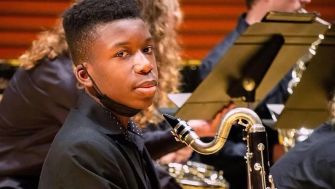 A Black teenager playing a musical instrument in a school band setting.
